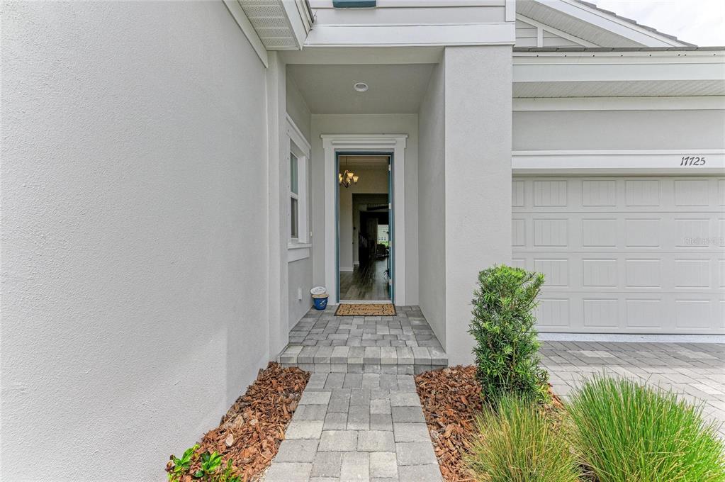 The exterior view shows a paved walkway leading to a covered front entryway and garage — 17725 ROOST PLACE, LAKEWOOD RANCH, FL