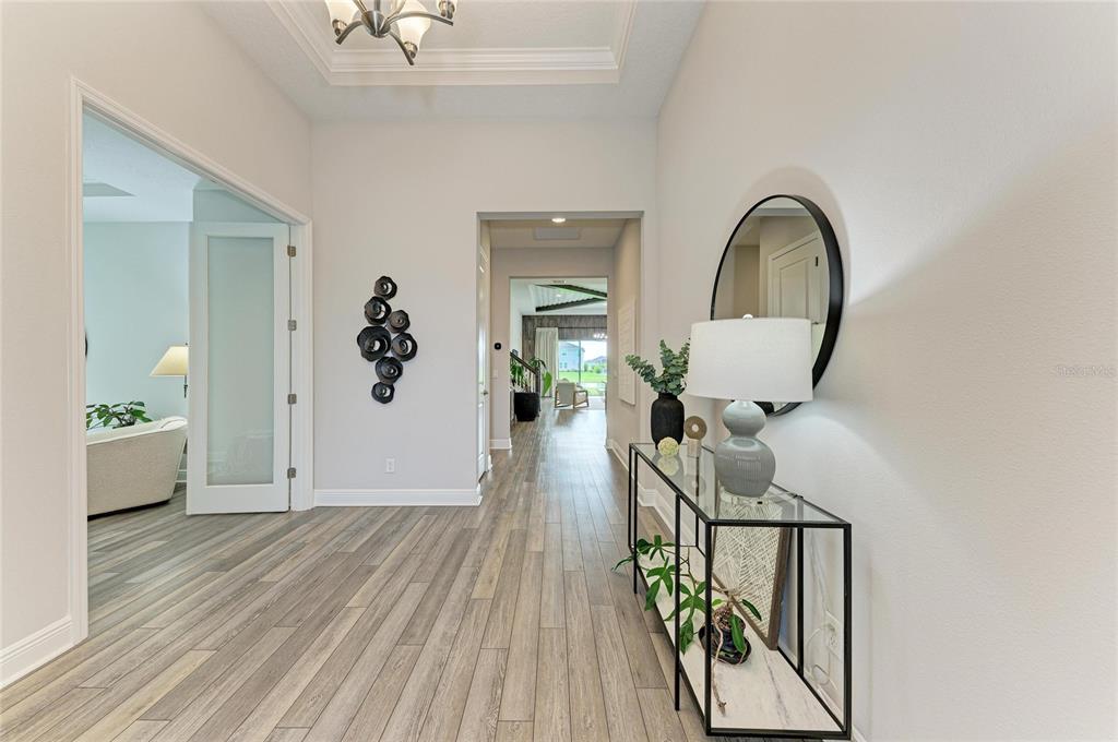 A bright foyer features light wood-look flooring, a glass console table, and a circular mirror — 17725 ROOST PLACE, LAKEWOOD RANCH, FL