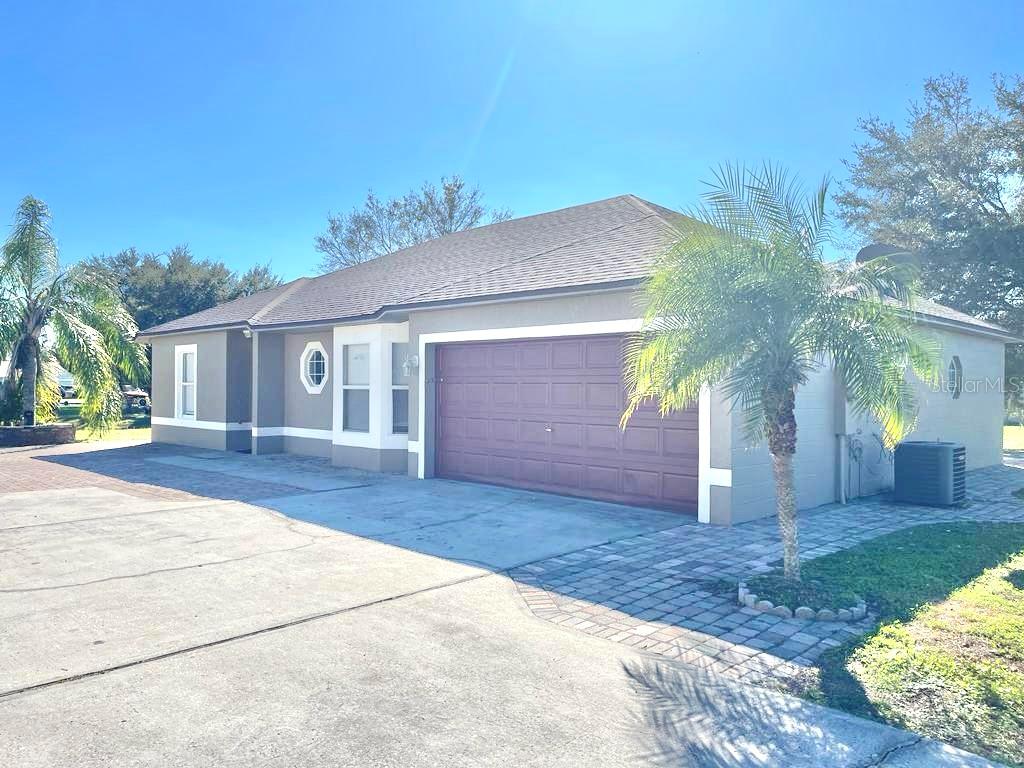 A single-story house with a two-car garage, a paved driveway, and a palm tree — 221 COBALT DRIVE, KISSIMMEE, FL