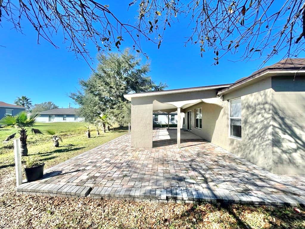 A paved patio sits beside a house with a covered porch and a grassy yard — 221 COBALT DRIVE, KISSIMMEE, FL