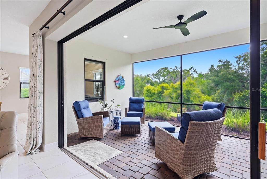 A screened-in patio features wicker chairs with blue cushions, brick flooring, and a ceiling fan — 13231 INDIGO WAY, BRADENTON, FL
