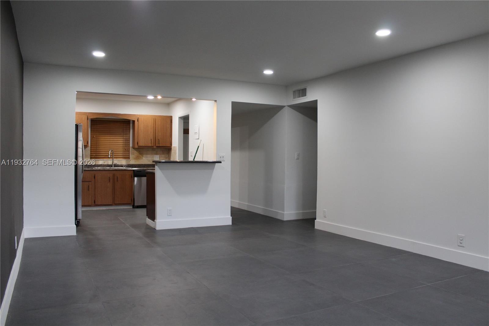A living area with large gray floor tiles leads to a kitchen with wood cabinets — 5140 SW 40th Ave # 3C, Dania Beach FL 33314, DANIA BEACH, FL