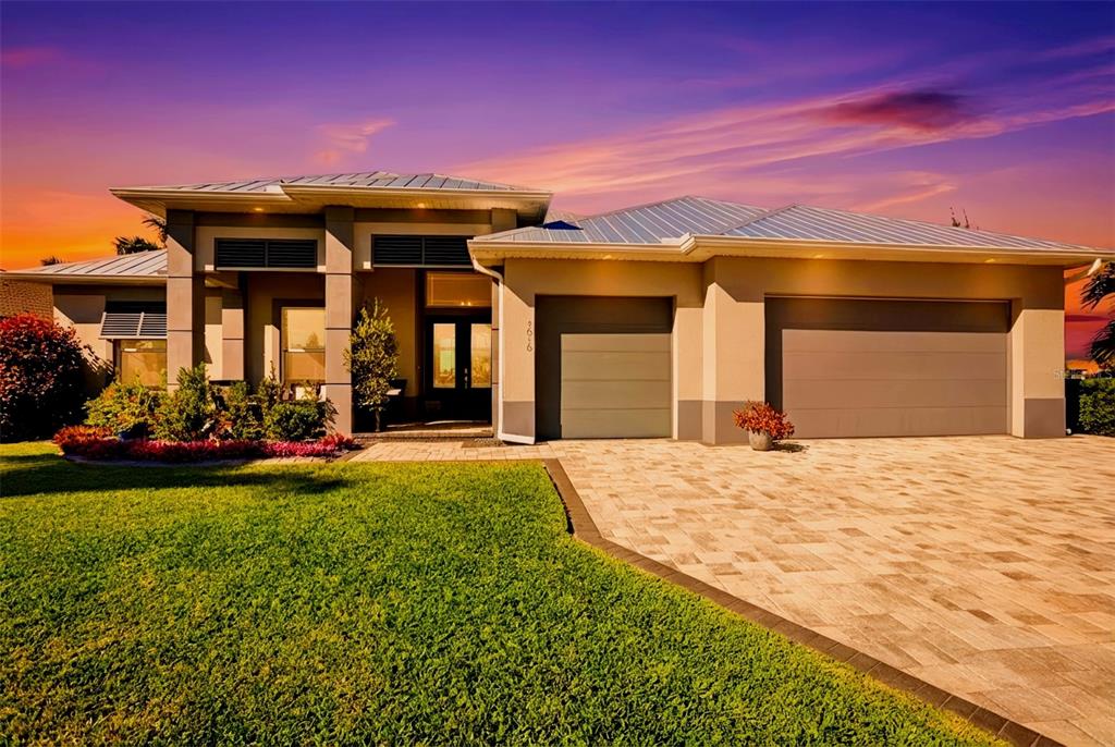 A modern single-story house with a metal roof, two garage doors, and a paved driveway — 1616 N OLD BURNT STORE ROAD N, CAPE CORAL, FL