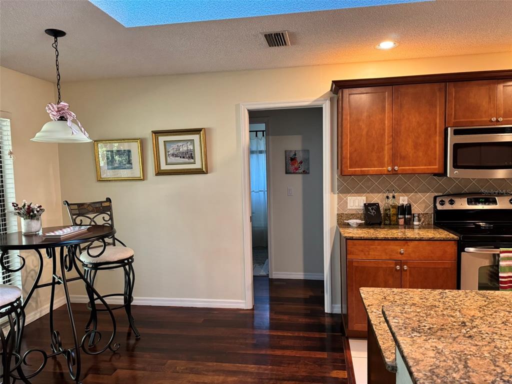 A kitchen with wood cabinets, granite countertops, and an adjacent dining area with a bistro table — 4487 TRAILS DRIVE, SARASOTA, FL