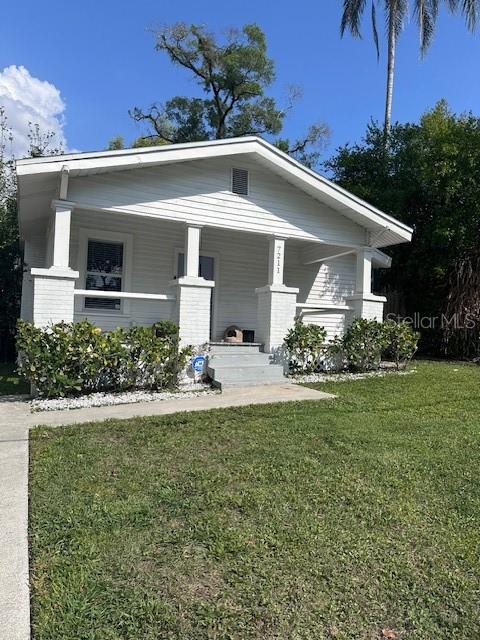 A white, single-story house with a front porch and steps sits on a grassy lawn — 7211 N TALIAFERRO AVENUE, TAMPA, FL