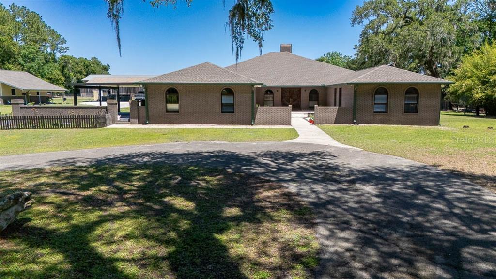 A single-story brick house with arched windows and a paved driveway under large trees — 830 NW 111TH LANE, OXFORD, FL