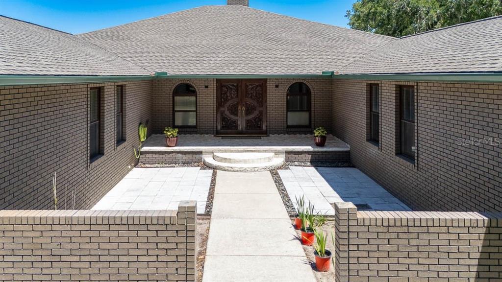 A brick house exterior features a central courtyard with a paved walkway and double front doors — 830 NW 111TH LANE, OXFORD, FL