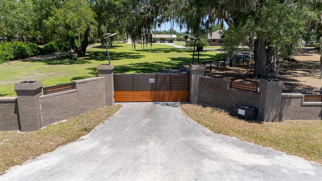 A brick wall with a large wooden gate marks the entrance to a wooded property — 830 NW 111TH LANE, OXFORD, FL