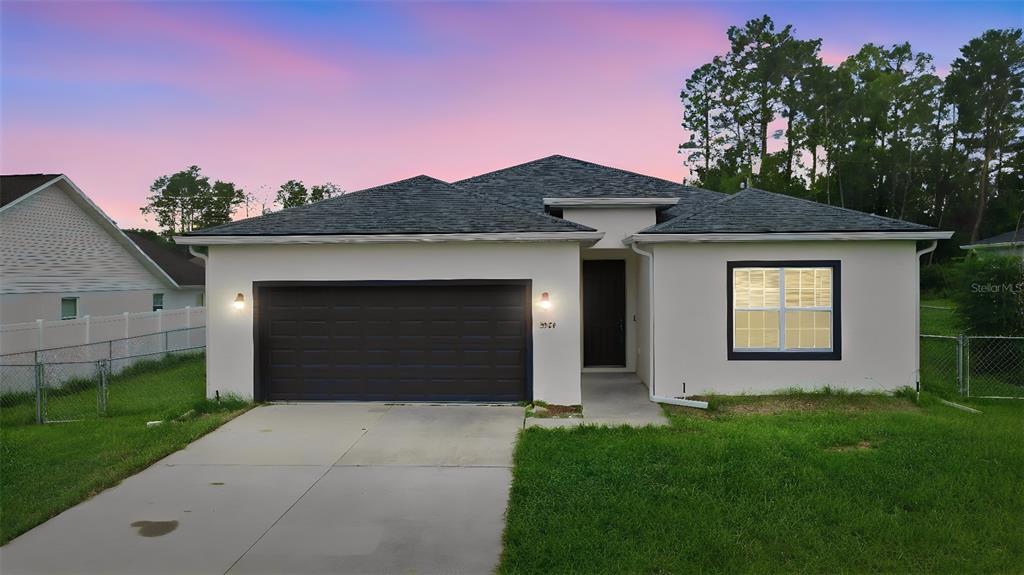 A single-story house with a dark garage door, white stucco exterior, and a concrete driveway — 5574 SW 128TH PLACE, OCALA, FL