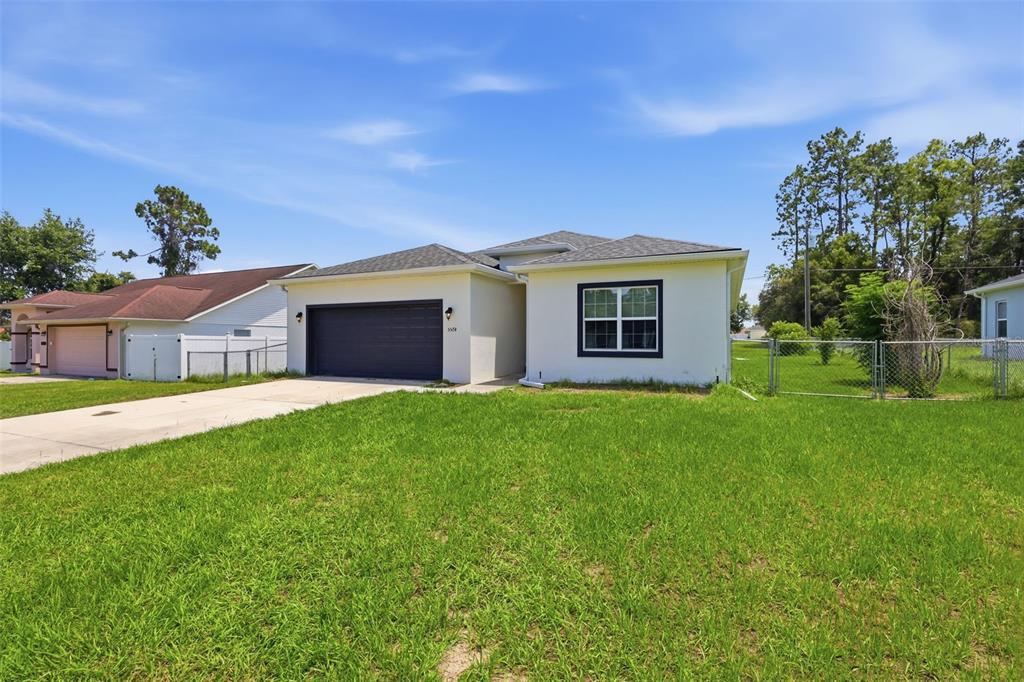 A single-story house with a white stucco exterior, dark garage door, and a grassy lawn — 5574 SW 128TH PLACE, OCALA, FL