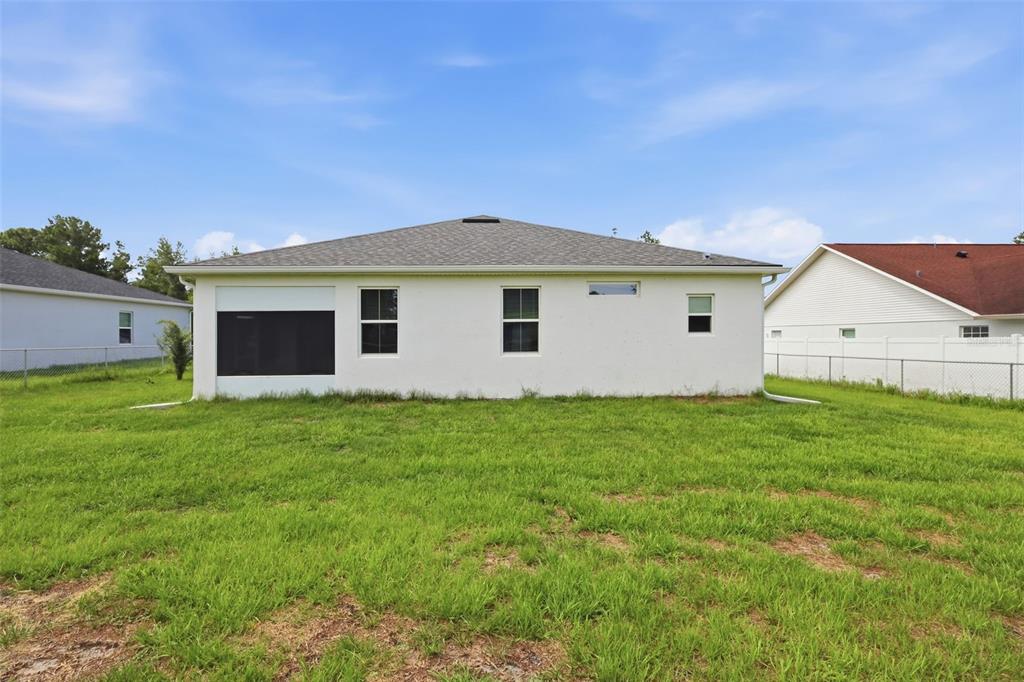 The rear exterior of a white single-story house features a screened-in porch and grass yard — 5574 SW 128TH PLACE, OCALA, FL
