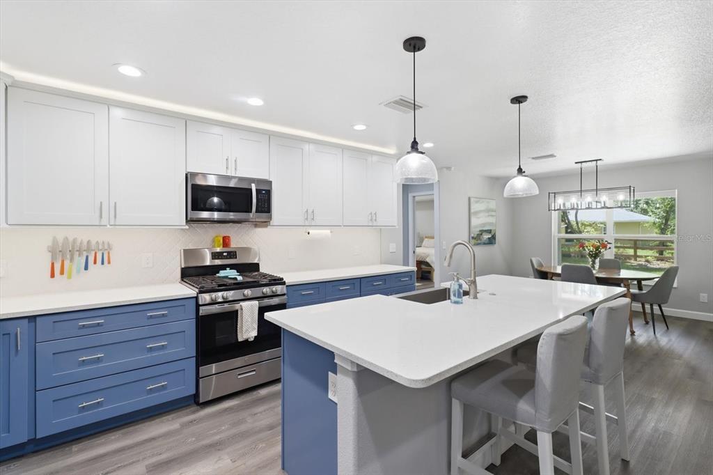 A kitchen features blue lower cabinets, white upper cabinets, a central island, and dining area — 232 E FALCON STREET, DUNNELLON, FL