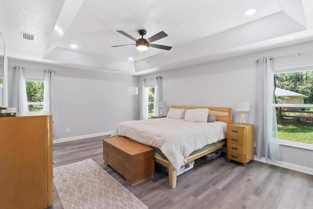 A bedroom features a tray ceiling, ceiling fan, light wood furniture, and gray flooring — 232 E FALCON STREET, DUNNELLON, FL