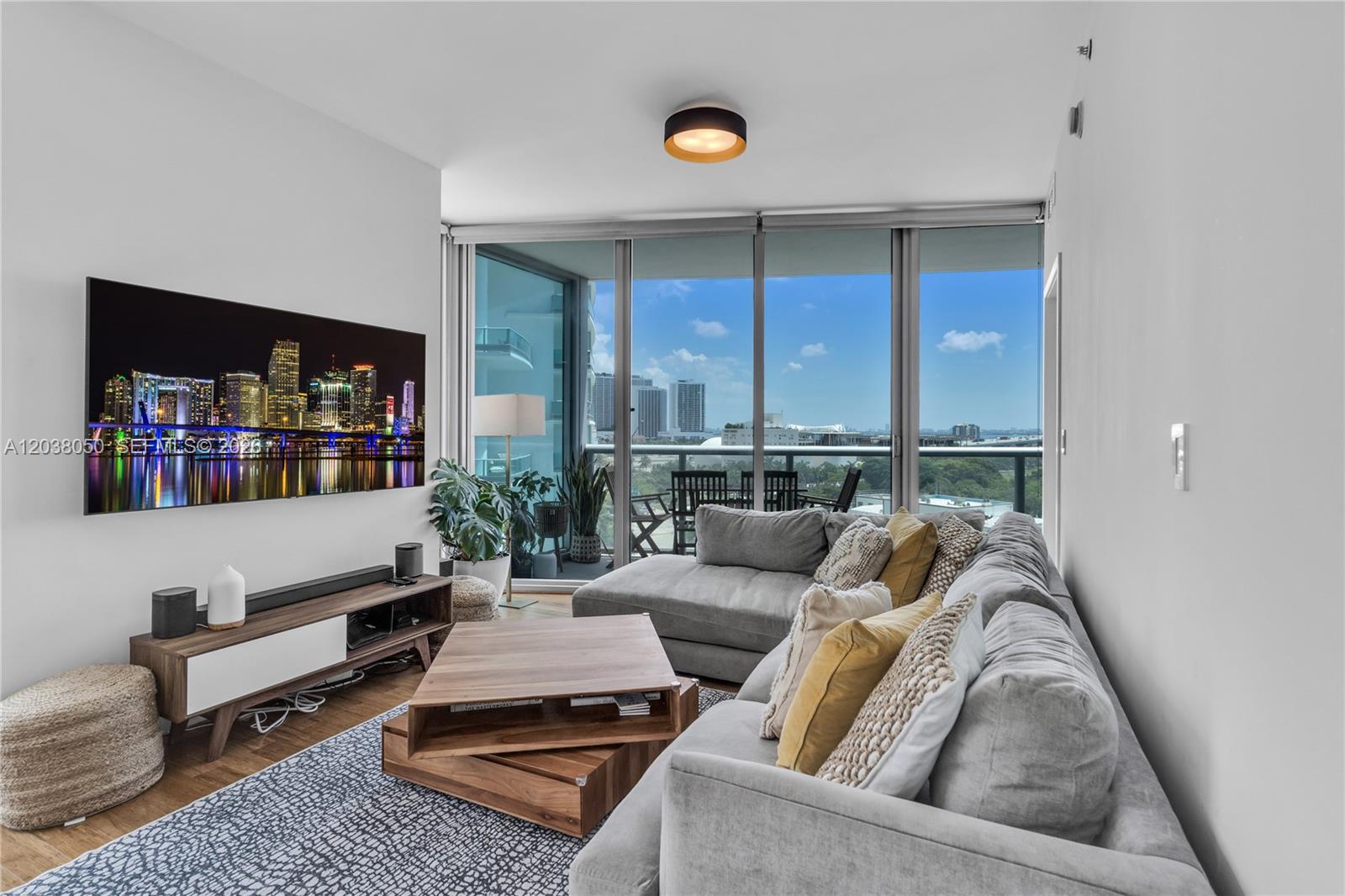 A living room features a large sectional sofa, a wooden coffee table, and floor-to-ceiling windows — 888 Biscayne Boulevard # 812, Miami FL 33132, MIAMI, FL