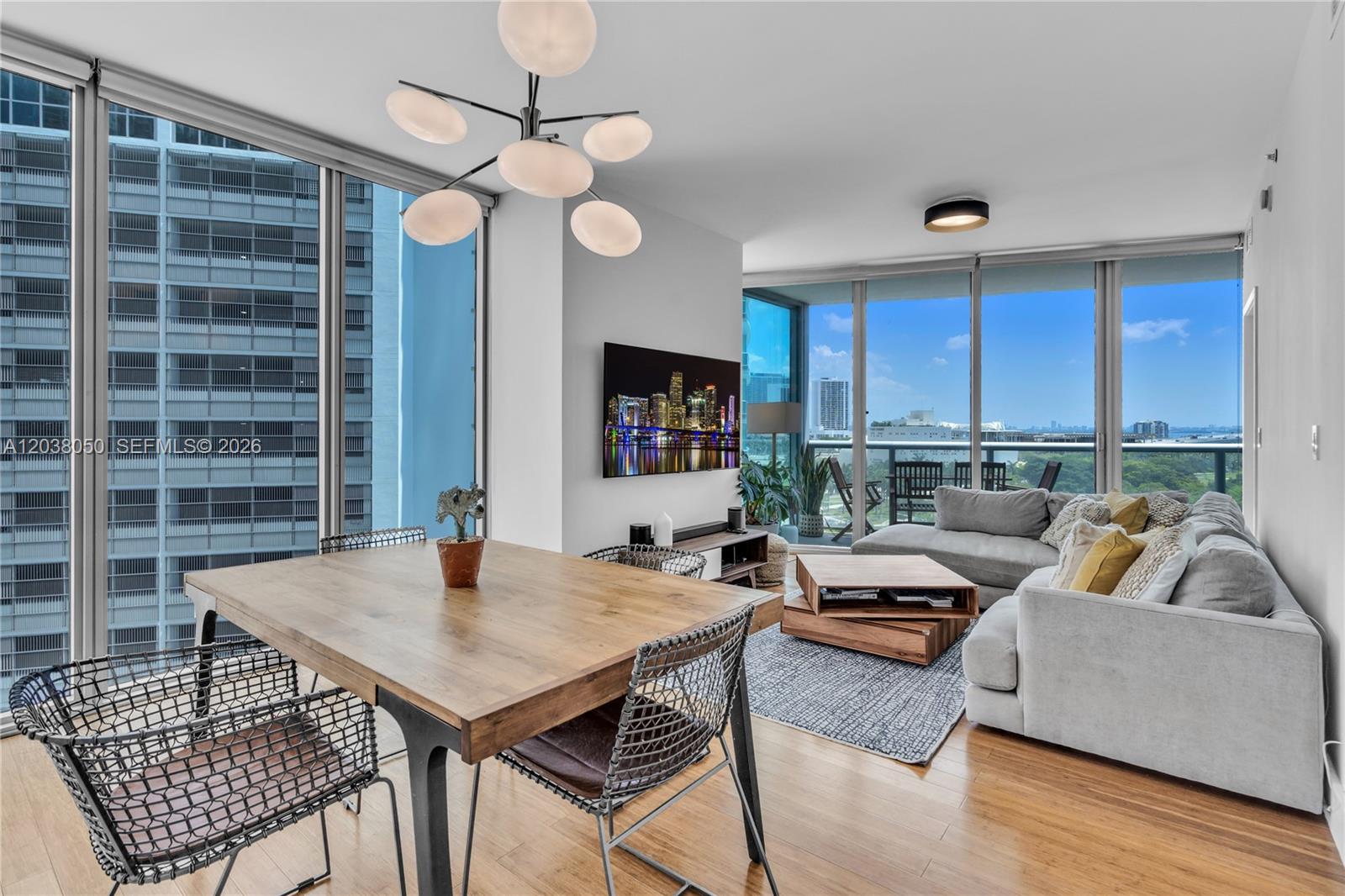 A modern living and dining area features floor-to-ceiling windows, hardwood floors, and a balcony — 888 Biscayne Boulevard # 812, Miami FL 33132, MIAMI, FL