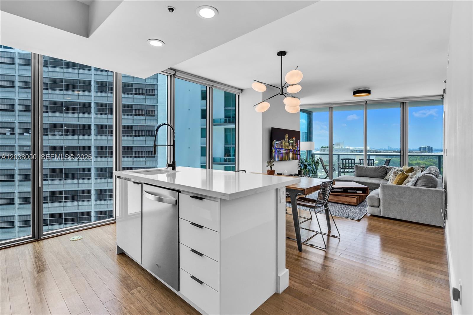 A modern kitchen island with a stainless steel dishwasher faces a living area with floor-to-ceiling windows — 888 Biscayne Boulevard # 812, Miami FL 33132, MIAMI, FL