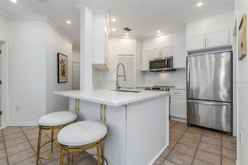 A white kitchen features a marble-topped island, stainless steel appliances, and gold cabinet hardware — 2199 CHIANTI PLACE UNIT 9-0923, PALM HARBOR, FL