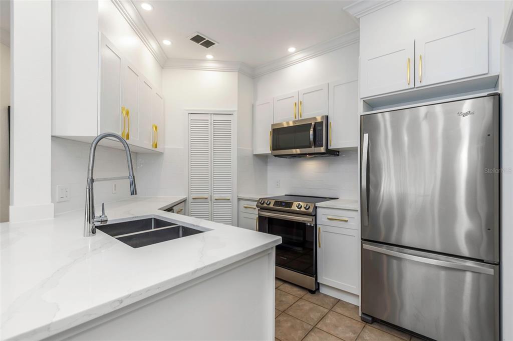 A kitchen features white cabinets, stainless steel appliances, gold hardware, and white quartz countertops — 2199 CHIANTI PLACE UNIT 9-0923, PALM HARBOR, FL