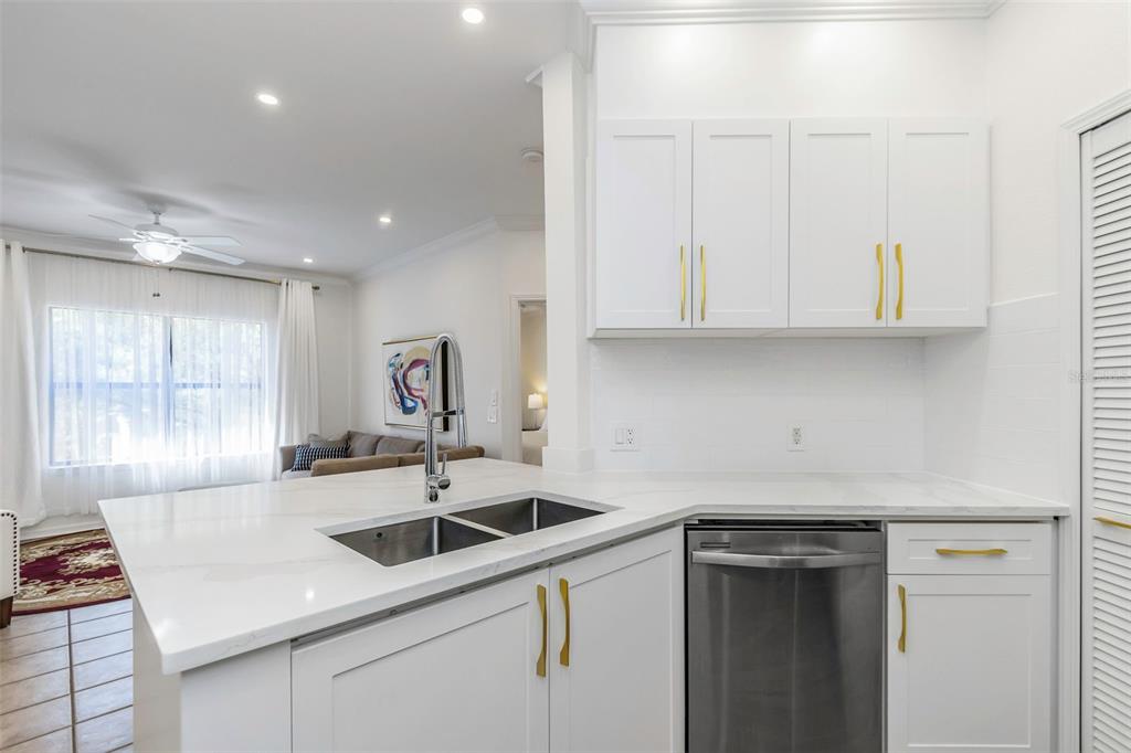 A bright kitchen features white cabinets, gold hardware, a stainless steel dishwasher, and quartz countertops — 2199 CHIANTI PLACE UNIT 9-0923, PALM HARBOR, FL