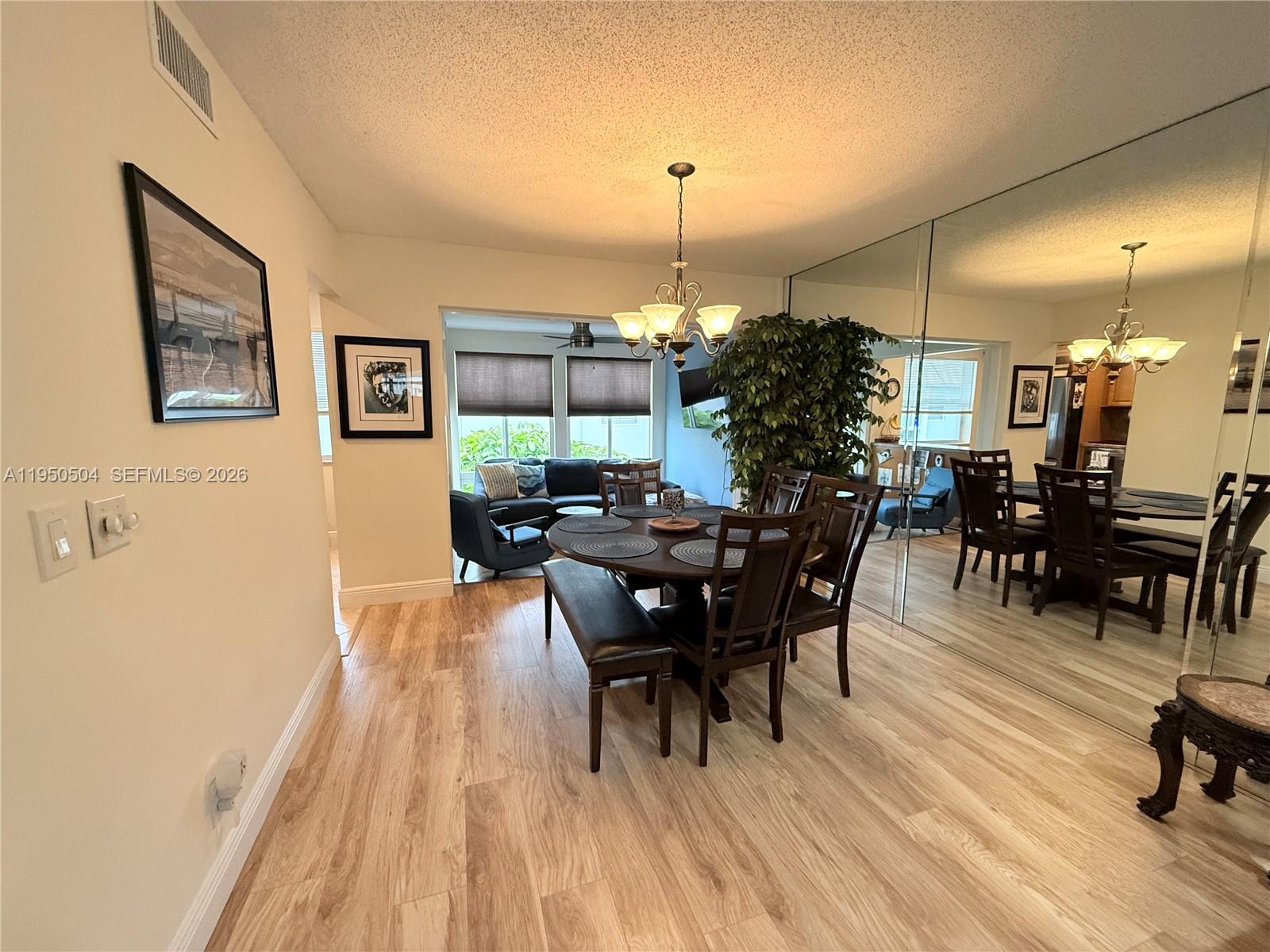 A dining area features a round wooden table, chairs, a bench, and a large mirrored wall — 18 Colonial Club Dr # 202, Boynton Beach FL 33435, BOYNTON BEACH, FL