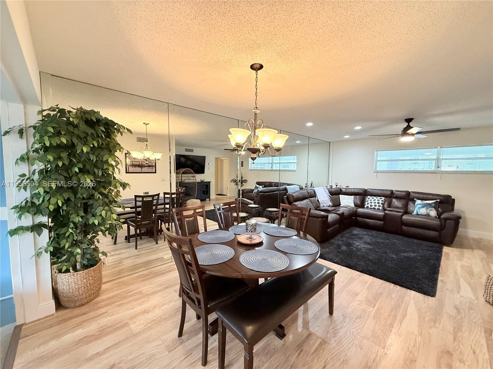 A dining area and living room feature wood-look flooring, a mirrored wall, and a chandelier — 18 Colonial Club Dr # 202, Boynton Beach FL 33435, BOYNTON BEACH, FL
