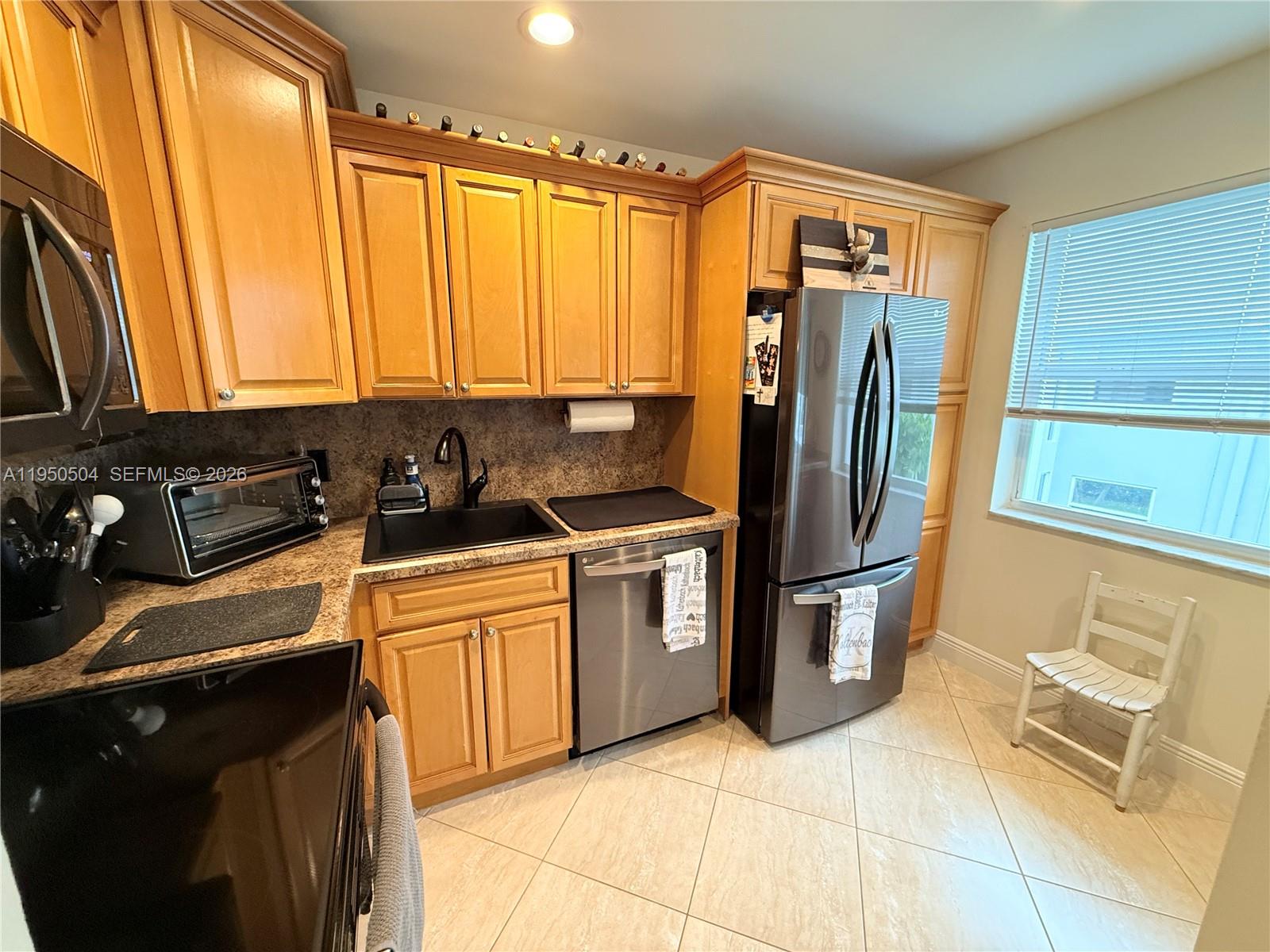 A kitchen features light wood cabinets, stainless steel appliances, a black sink, and tile flooring — 18 Colonial Club Dr # 202, Boynton Beach FL 33435, BOYNTON BEACH, FL