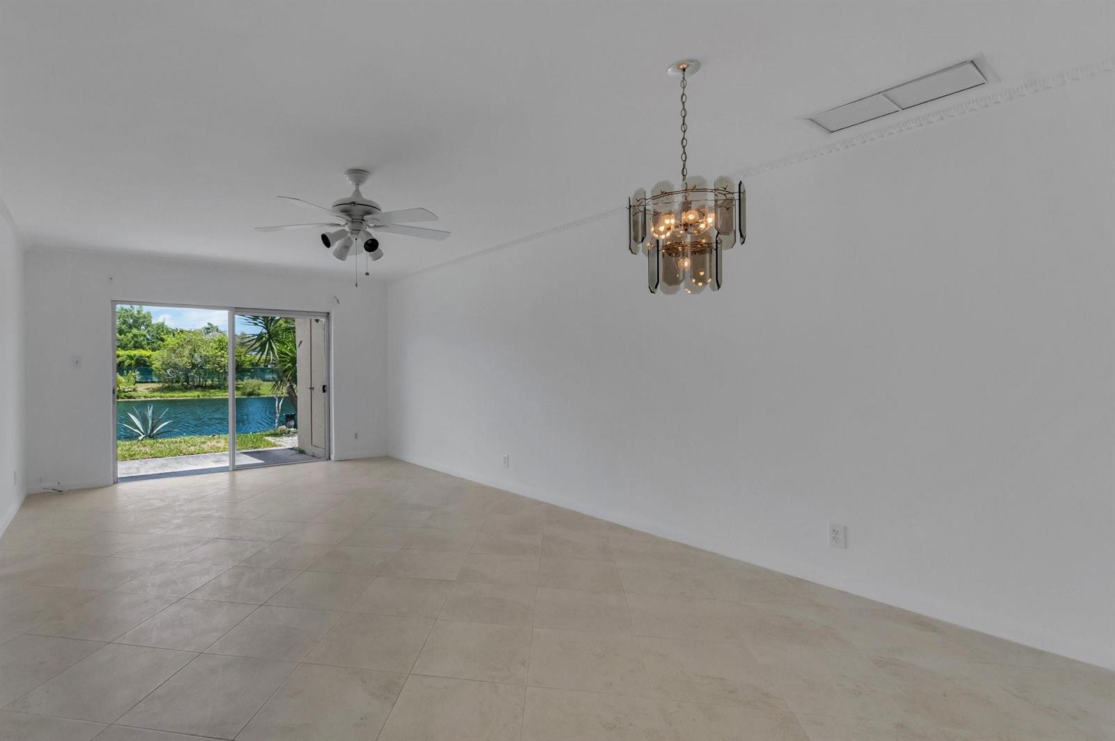 An empty room with tile floors, a ceiling fan, a chandelier, and sliding glass doors — 8829 Bella Vista Drive # 282, Boca Raton FL 33433, BOCA RATON, FL