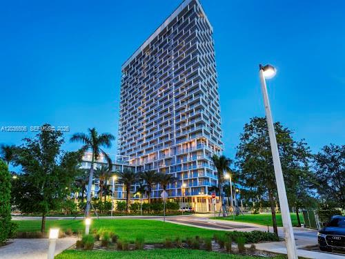 A tall modern residential high-rise building stands behind a landscaped lawn with palm trees — 2000 Metropica Way # 2610, Sunrise FL 33323, SUNRISE, FL