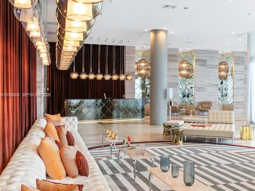 A modern hotel lobby features a long tufted sofa, pendant lighting, and a reception desk — 2000 Metropica Way # 2610, Sunrise FL 33323, SUNRISE, FL