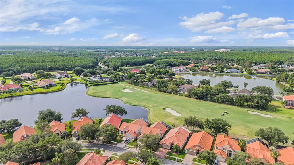 An aerial view shows a residential neighborhood with orange-roofed houses bordering a golf course and lake — 18911 AVENUE BIARRITZ, LUTZ, FL