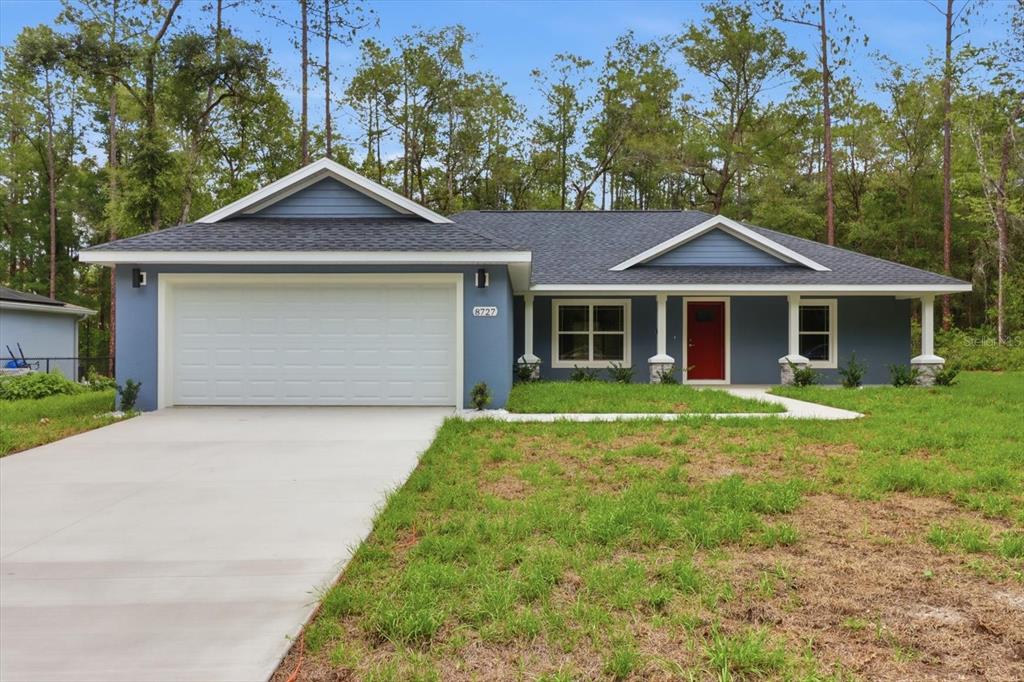 A blue single-story house with a white garage door, red front door, and pine trees — 8727 N SPIKES WAY, DUNNELLON, FL