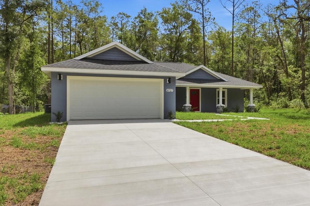 A single-story blue house with a two-car garage and a red front door — 8727 N SPIKES WAY, DUNNELLON, FL