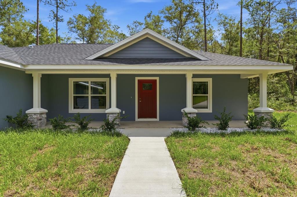 A blue house with a red front door, a covered porch, and a concrete walkway — 8727 N SPIKES WAY, DUNNELLON, FL