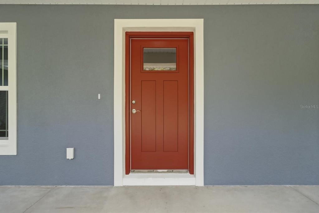 A red front door with a small window is centered on a gray exterior wall — 8727 N SPIKES WAY, DUNNELLON, FL