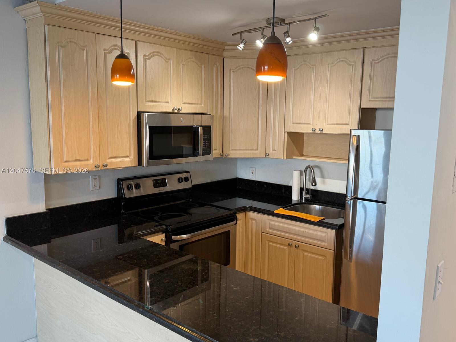 A kitchen features light wood cabinets, black granite countertops, and stainless steel appliances — 1990 Marseille Dr # 303, Miami Beach FL 33141, MIAMI BEACH, FL