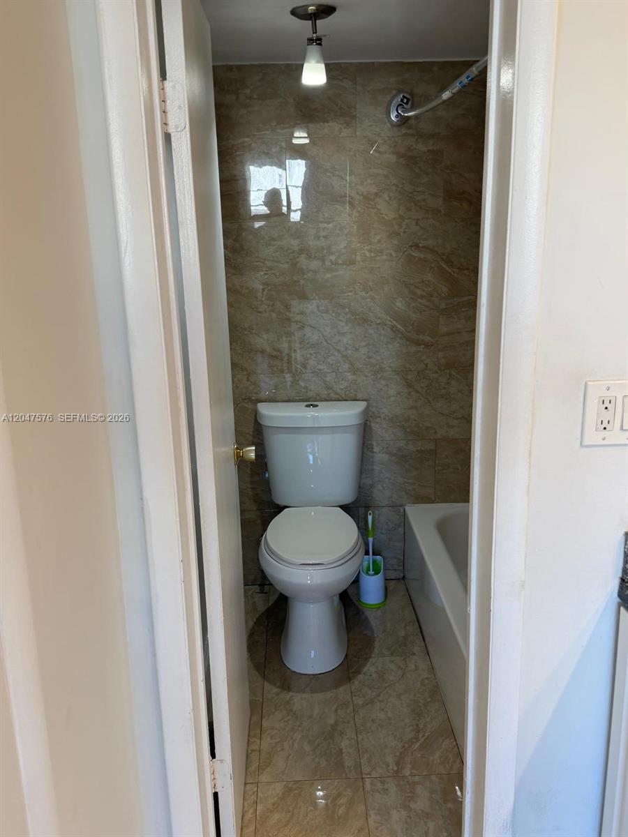 A small bathroom features a toilet, a bathtub, and tan tile walls and flooring — 1990 Marseille Dr # 303, Miami Beach FL 33141, MIAMI BEACH, FL