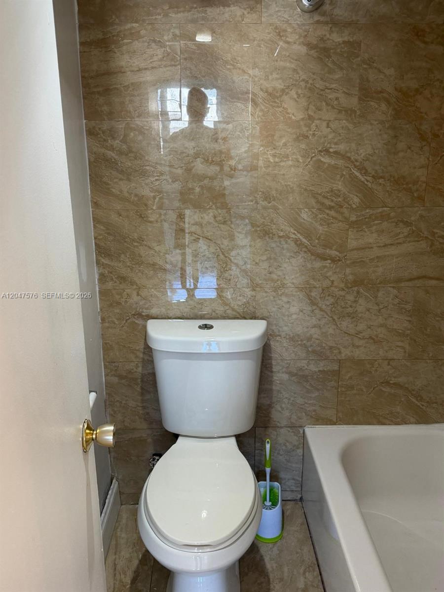 A bathroom features a white toilet, a bathtub, and beige marble-patterned wall tiles — 1990 Marseille Dr # 303, Miami Beach FL 33141, MIAMI BEACH, FL