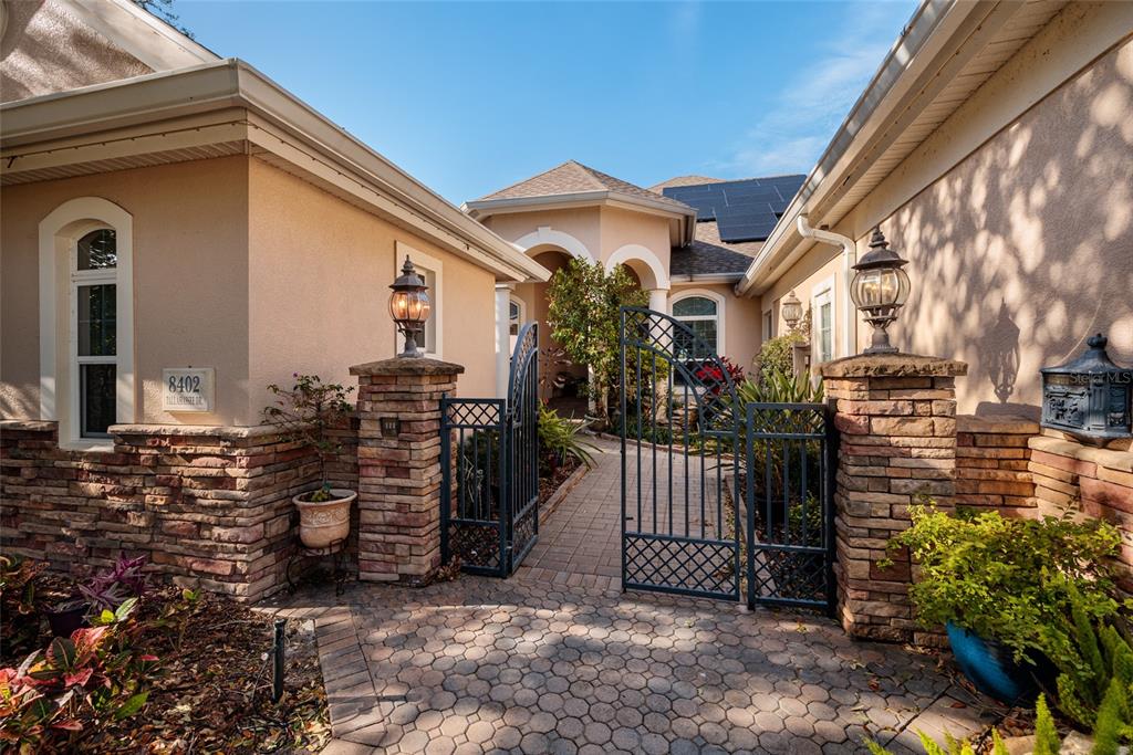A paved walkway leads through a metal gate to the front entrance of a house — 8402 TALLAHASSEE DRIVE NE, ST PETERSBURG, FL