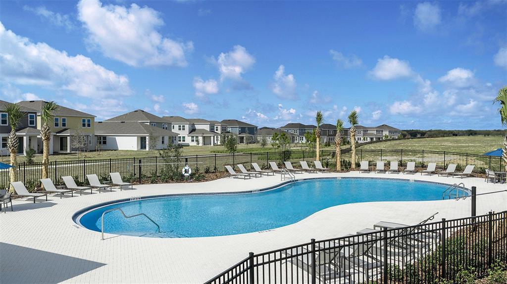 A swimming pool with lounge chairs sits in front of a residential neighborhood under clouds — 515 MOONSTONE COURT, GROVELAND, FL