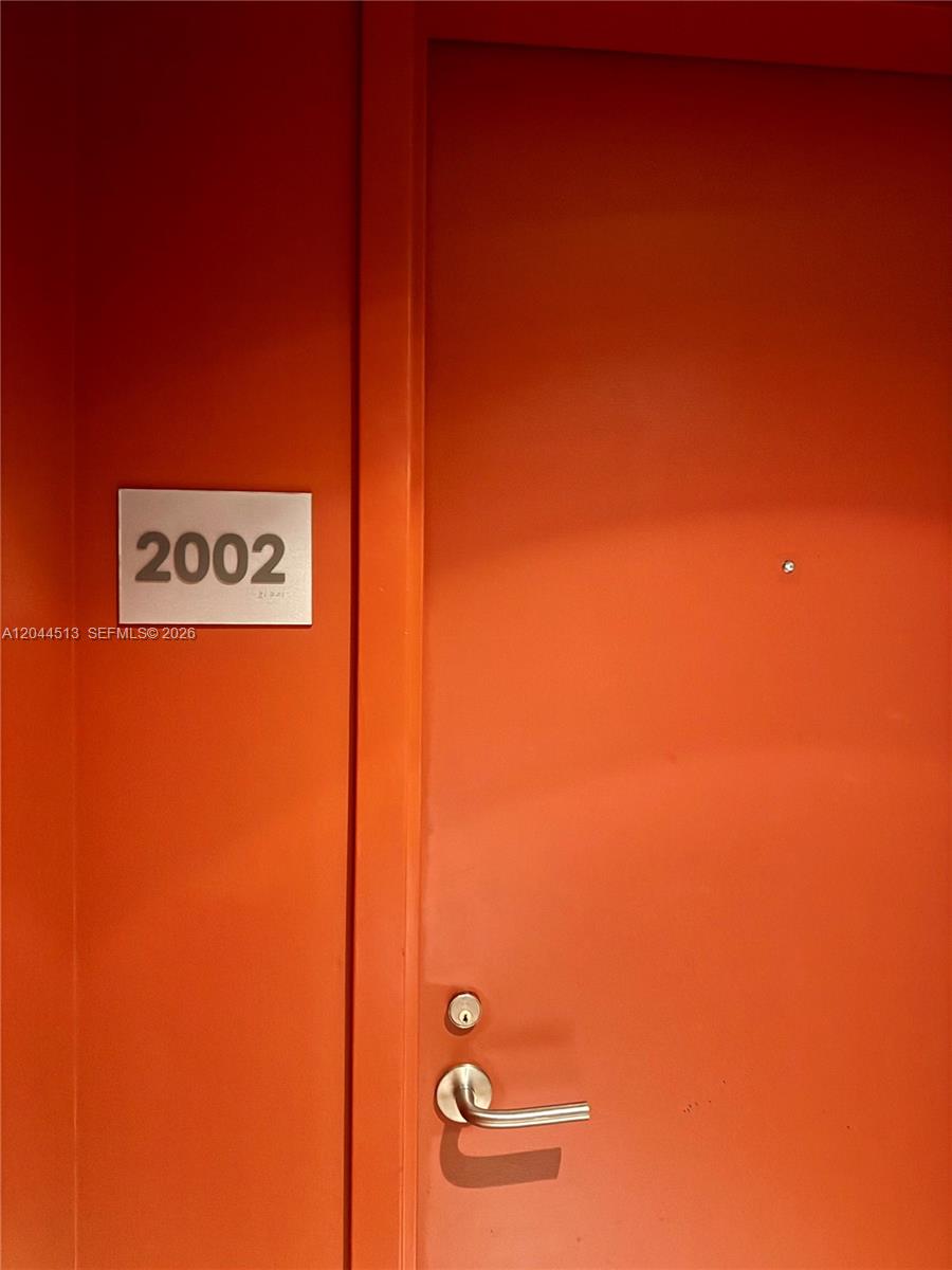 A bright orange door features a silver handle and a sign labeled 2002 — 1100 S Miami Ave # 2002, Miami FL 33130, MIAMI, FL