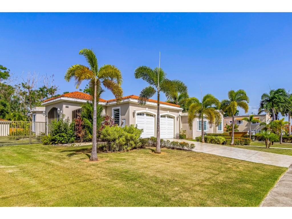 A single-story house with a tiled roof, two garage doors, and several palm trees — A3 PASEO MADRID, VEGA ALTA, PR