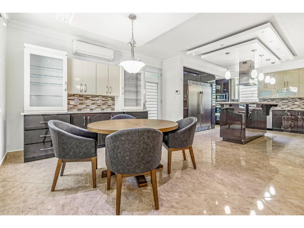 A dining area with a round wooden table and chairs sits adjacent to a modern kitchen — A3 PASEO MADRID, VEGA ALTA, PR