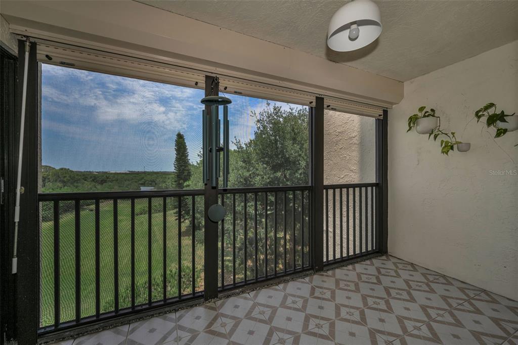 A screened-in balcony features tiled flooring, a ceiling light, and a view of greenery — 5400 PARK ST. NORTH UNIT 303, ST PETERSBURG, FL