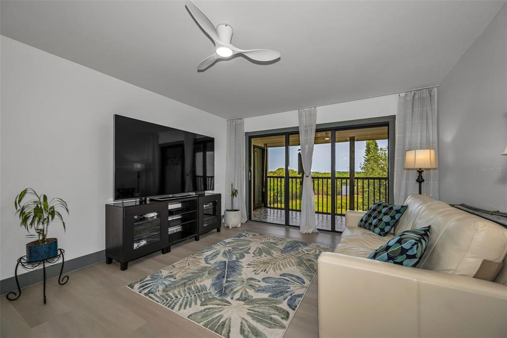A living room features a white sofa, a television on a stand, and sliding glass doors — 5400 PARK ST. NORTH UNIT 303, ST PETERSBURG, FL
