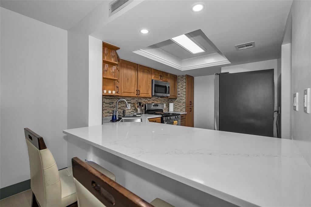 A kitchen features wood cabinets, a white quartz breakfast bar, and a black refrigerator — 5400 PARK ST. NORTH UNIT 303, ST PETERSBURG, FL