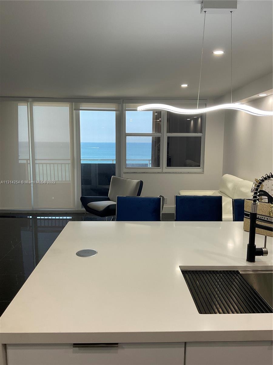 A modern kitchen island with a white countertop overlooks a living area with ocean views — 3180 S Ocean Dr # 1503, Hallandale Beach FL 33009, HALLANDALE BEACH, FL