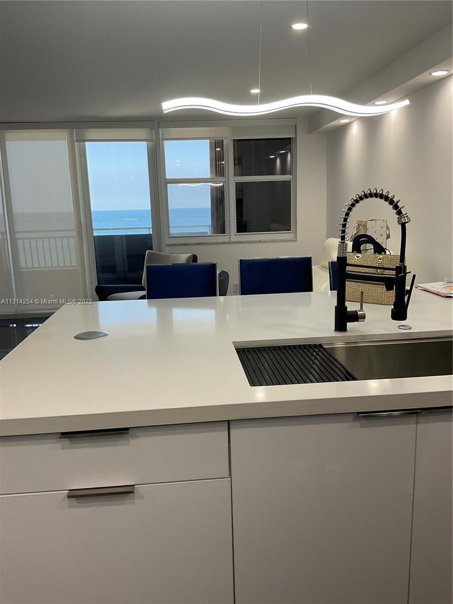 A modern kitchen island with a white countertop and black faucet overlooks a balcony view — 3180 S Ocean Dr # 1503, Hallandale Beach FL 33009, HALLANDALE BEACH, FL