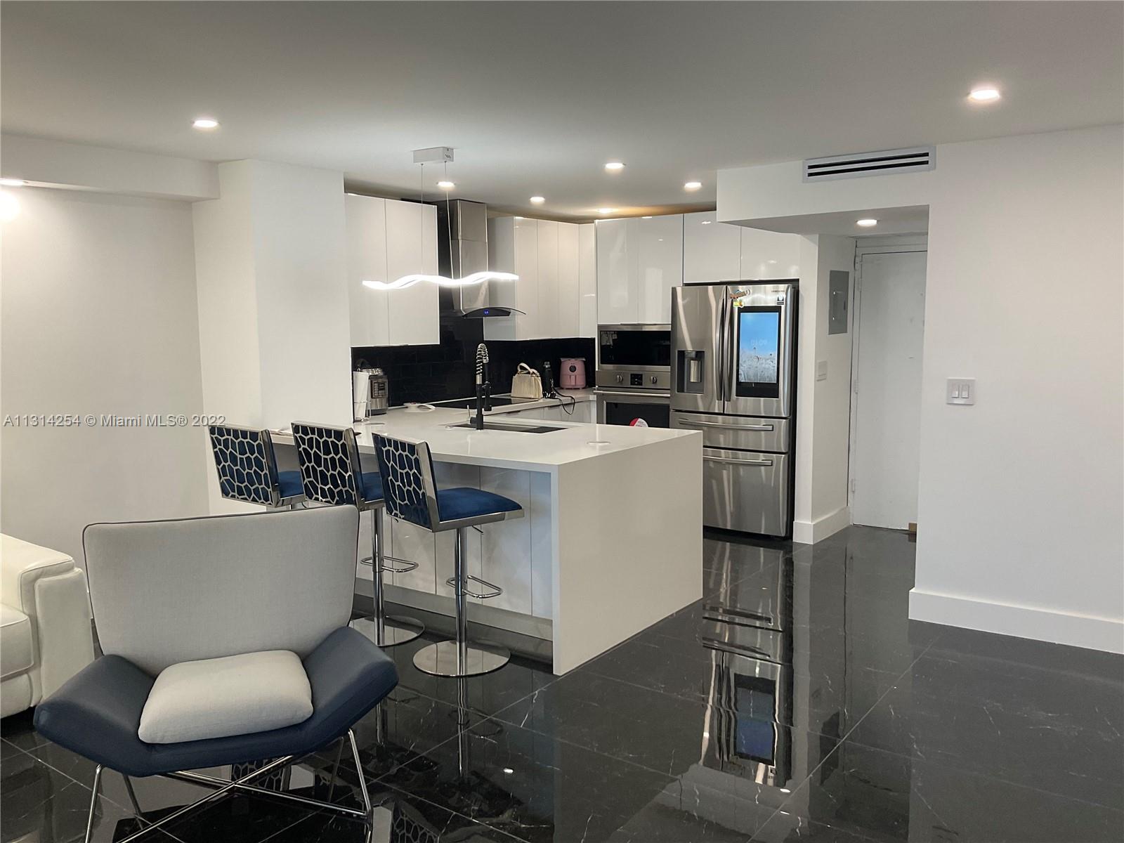 A modern kitchen features white cabinetry, a central island with bar stools, and black flooring — 3180 S Ocean Dr # 1503, Hallandale Beach FL 33009, HALLANDALE BEACH, FL