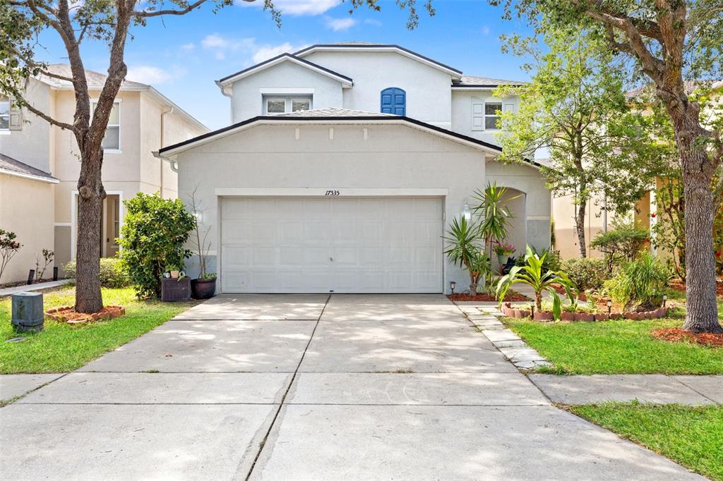A two-story suburban house features a two-car garage, light-colored stucco siding, and mature trees — 17535 BALMAHA DRIVE, LAND O LAKES, FL
