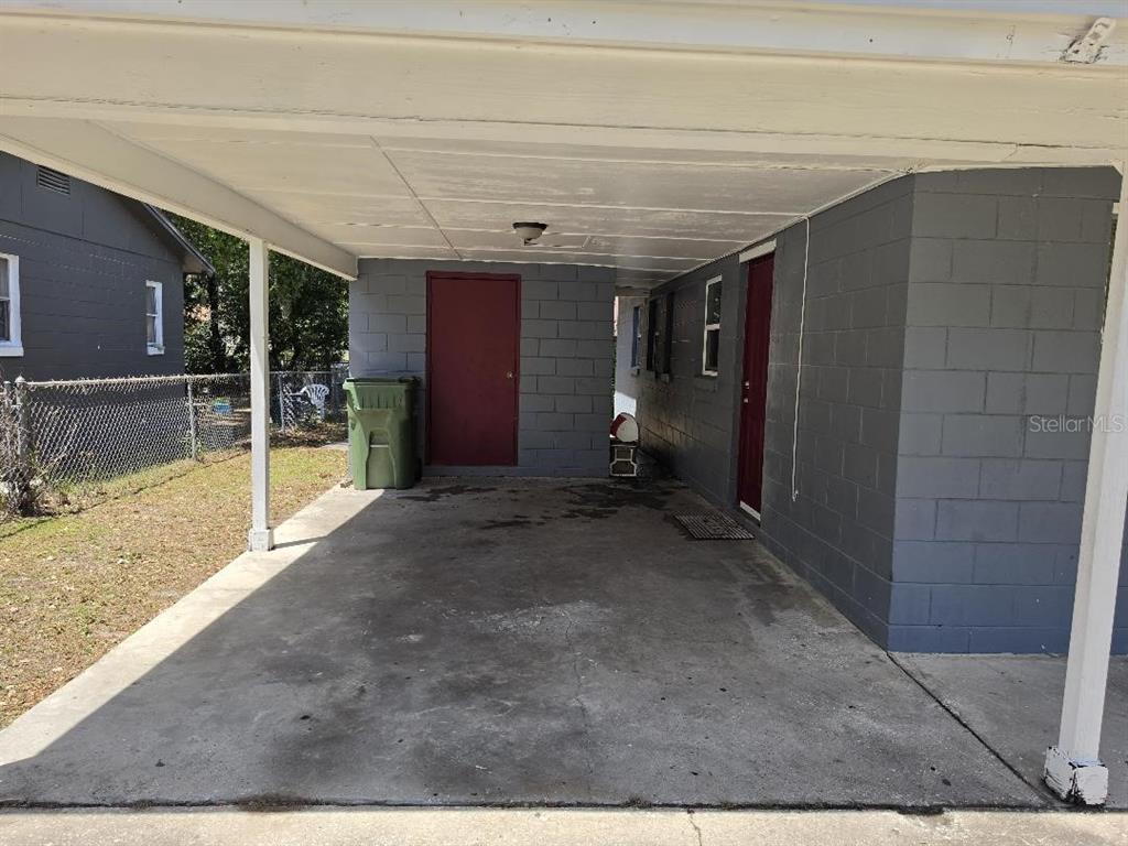 A covered concrete carport features gray block walls and two red exterior doors — 2316 MISPAH AVENUE, LEESBURG, FL